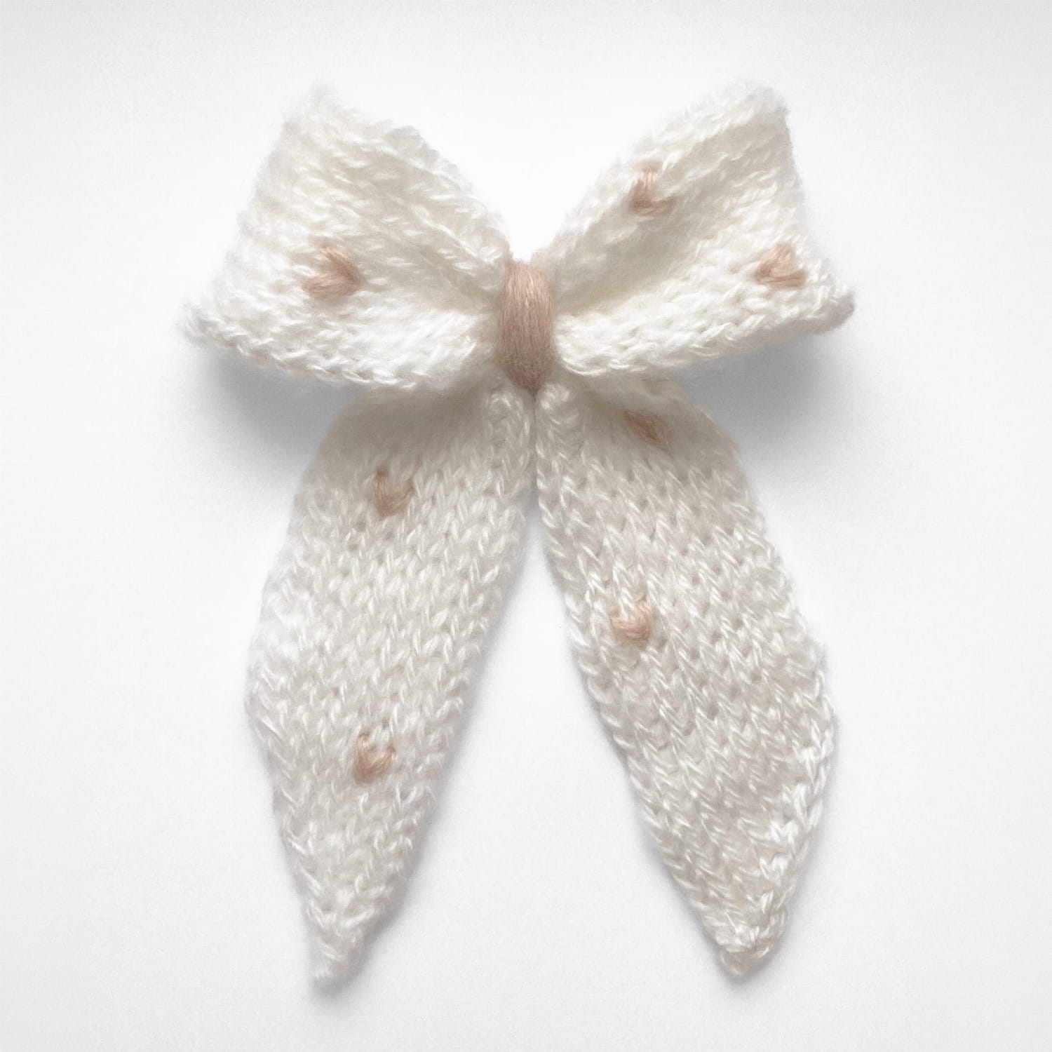 Ręcznie dziergana spinka do włosów w formie kokardy, widok z góry na jasnym tle.