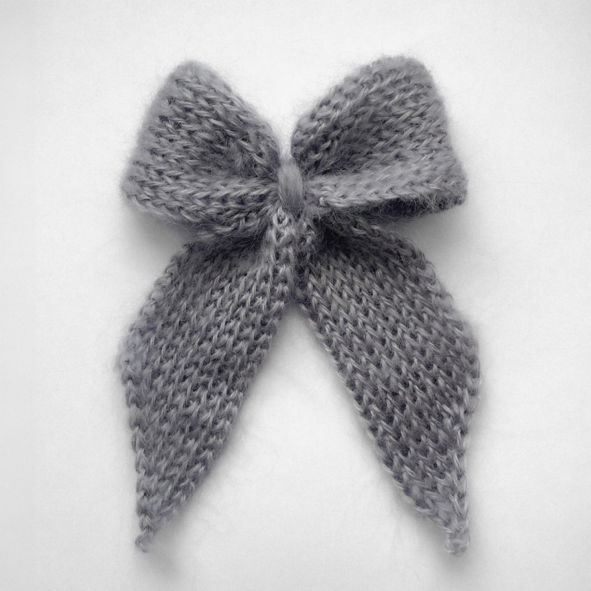 Ręcznie dziergana spinka do włosów w formie kokardy, widok z góry na jasnym tle.