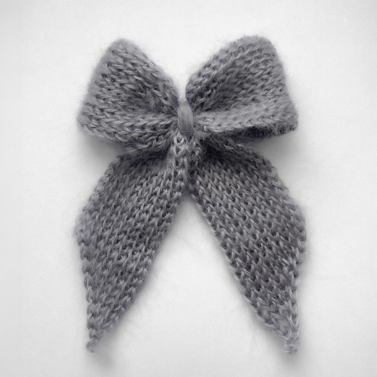 Ręcznie dziergana spinka do włosów w formie kokardy, widok z góry na jasnym tle.