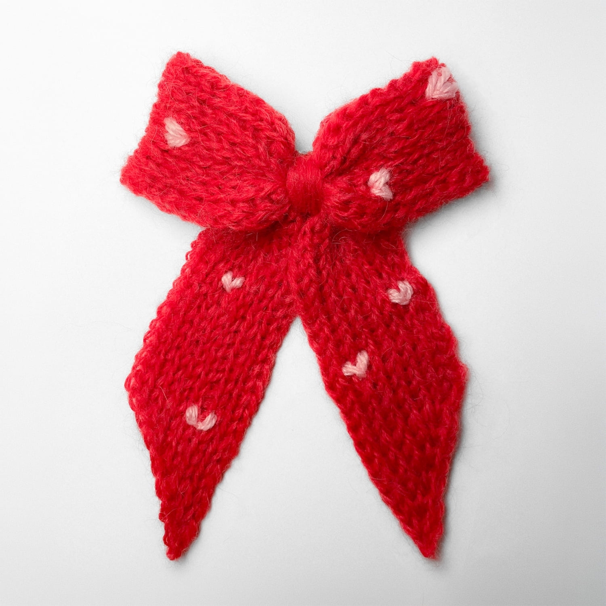 Ręcznie dziergana spinka do włosów w formie kokardy, widok z góry na jasnym tle.