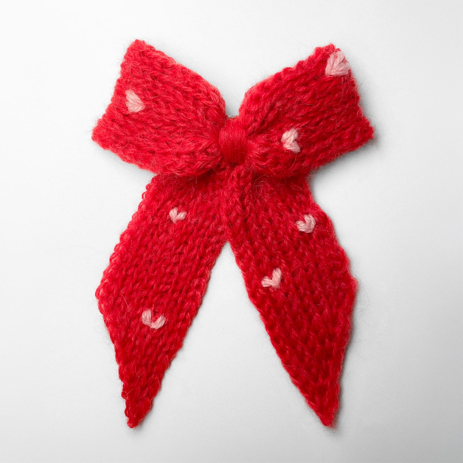 Ręcznie dziergana spinka do włosów w formie kokardy, widok z góry na jasnym tle.