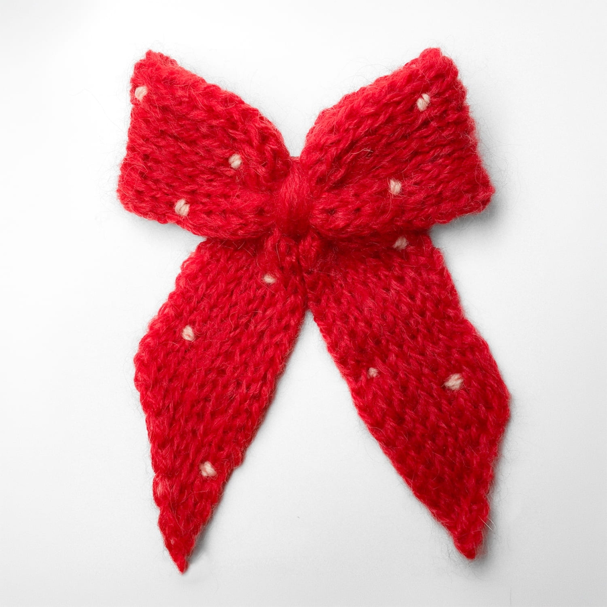 Ręcznie dziergana spinka do włosów w formie kokardy, widok z góry na jasnym tle.