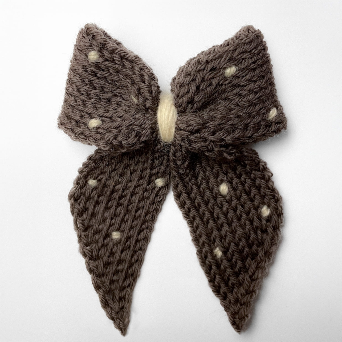 Ręcznie dziergana spinka do włosów w formie kokardy, widok z góry na jasnym tle.