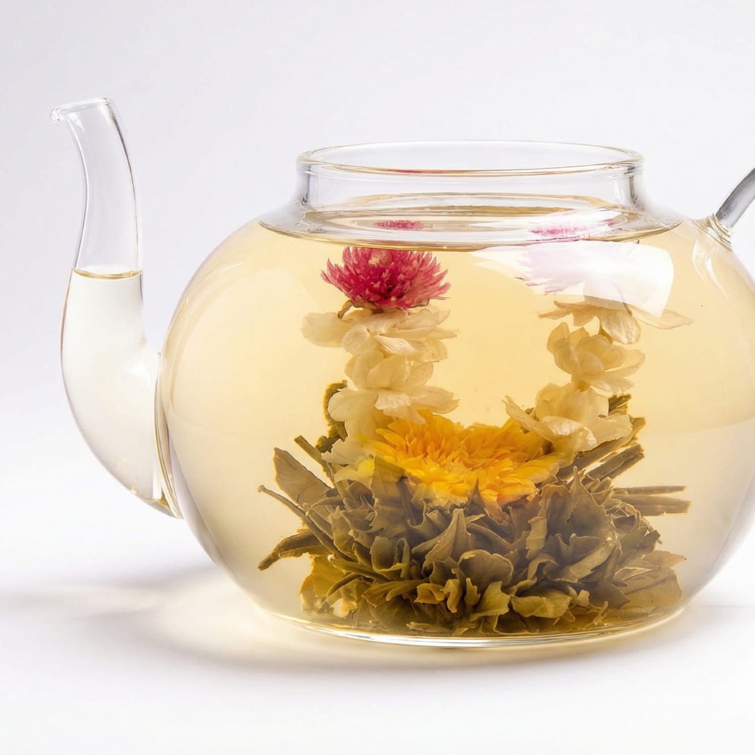 Kwitnąca herbata Sunset Love rozwijająca się w szklanym dzbanku z widocznymi kwiatami jaśminu, nagietka i gomfreny
